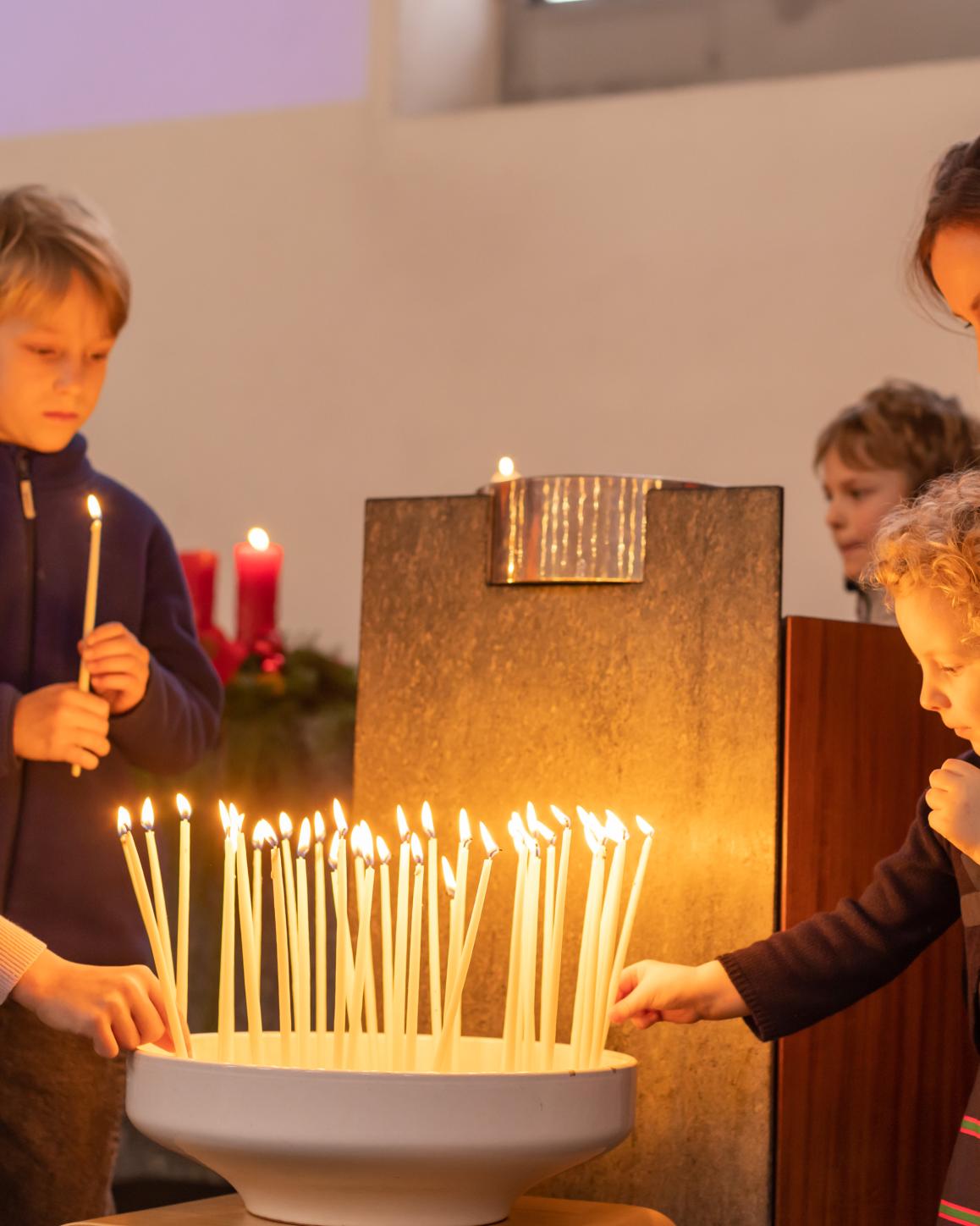 Kinder und eine Mutter zünden Kerzen an